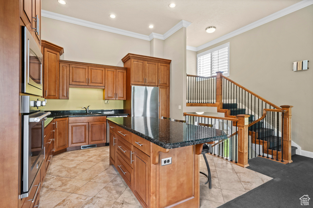 Kitchen featuring stainless steel appliances, crown molding, brown cabinetry, a center island, and a breakfast bar area