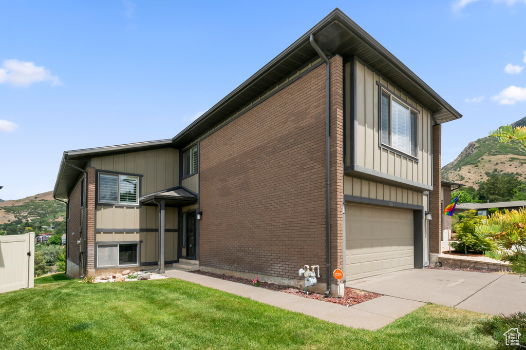 View of front of home featuring a mountain view, an attached garage, brick siding, a front yard, and board and batten siding