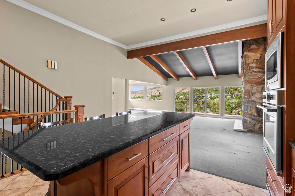 Kitchen with appliances with stainless steel finishes, light colored carpet, light tile patterned floors, dark stone counters, and brown cabinetry