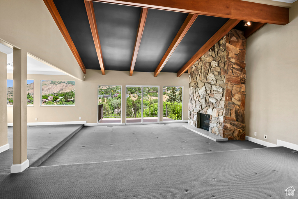 Unfurnished living room featuring carpet flooring, plenty of natural light, and a stone fireplace
