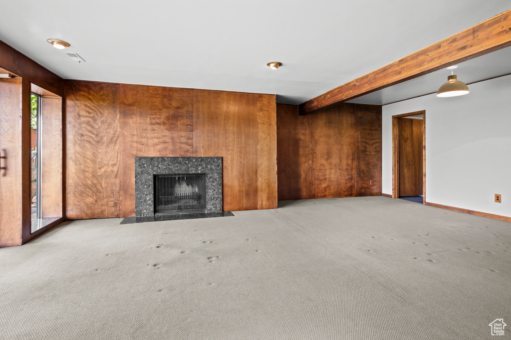 Unfurnished living room with carpet floors, a high end fireplace, beam ceiling, and wood walls