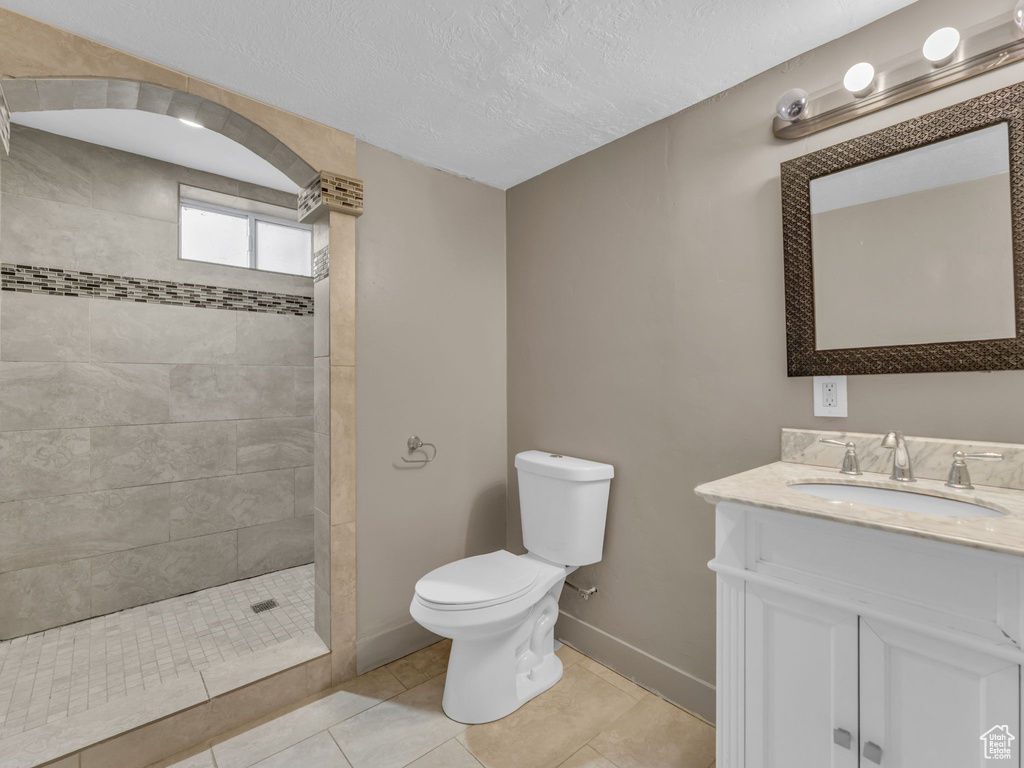 Bathroom with vanity, a tile shower, tile patterned flooring, and a textured ceiling