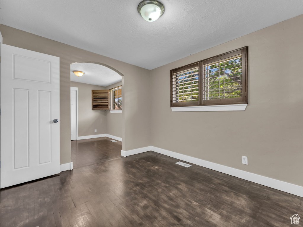 Unfurnished room with arched walkways, dark wood-style flooring, and a textured ceiling