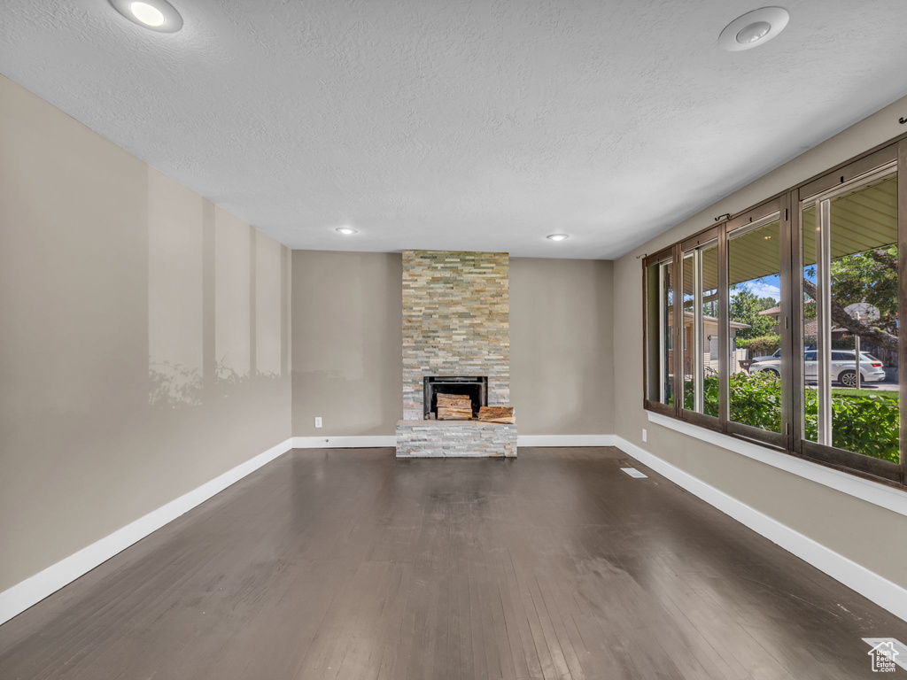 Unfurnished living room with a stone fireplace, a textured ceiling, dark wood finished floors, and recessed lighting