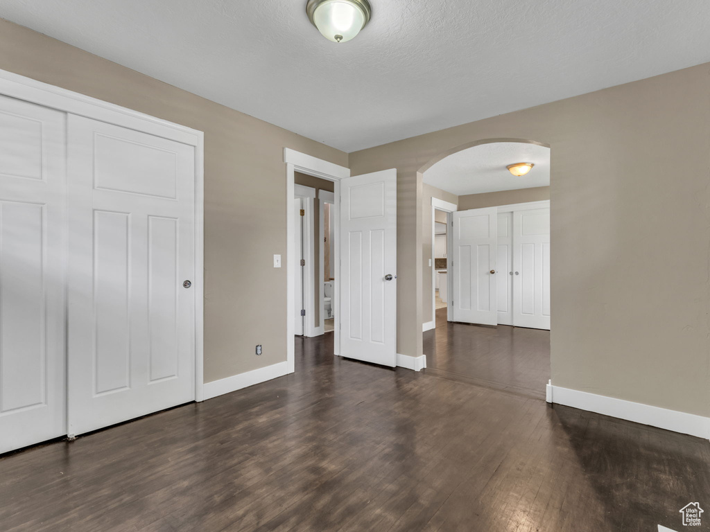 Unfurnished bedroom featuring arched walkways, wood finished floors, and a closet