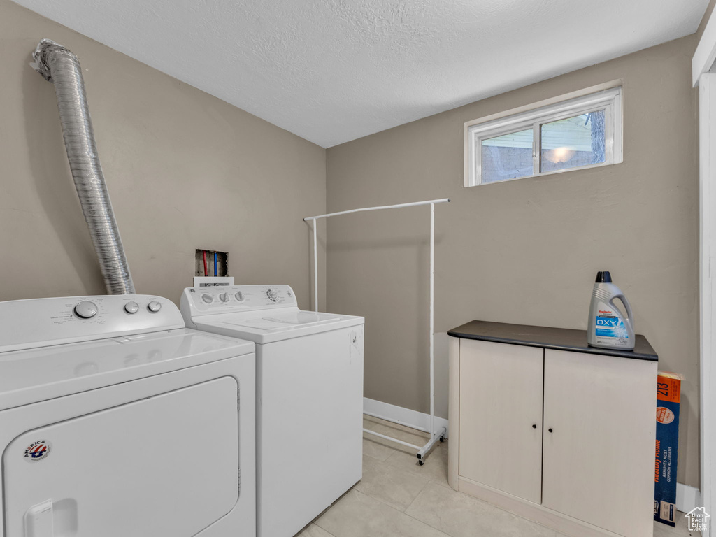 Laundry area with independent washer and dryer, light tile patterned flooring, and a textured ceiling