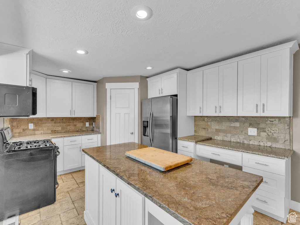 Kitchen featuring stainless steel refrigerator with ice dispenser, gas range oven, a center island, recessed lighting, and tasteful backsplash