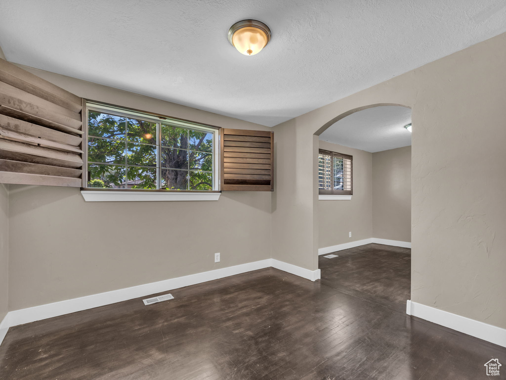 Spare room featuring arched walkways, wood finished floors, and a textured ceiling