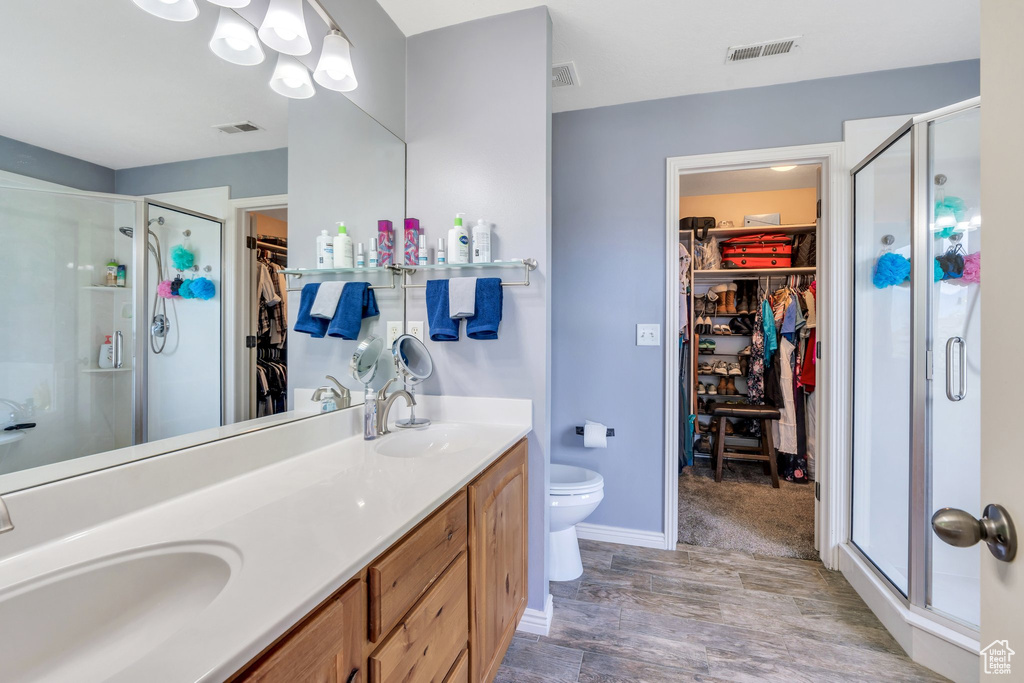 Full bath featuring a spacious closet, double vanity, a stall shower, and wood finished floors