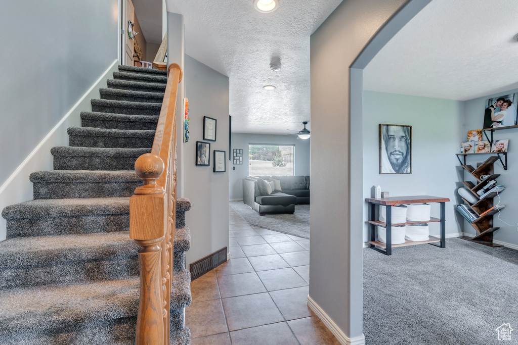 Stairway featuring a textured ceiling, arched walkways, tile patterned flooring, and a ceiling fan