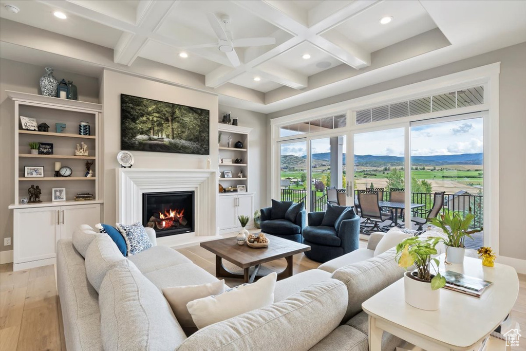 Living area with light wood-style flooring, coffered ceiling, a glass covered fireplace, recessed lighting, and beam ceiling