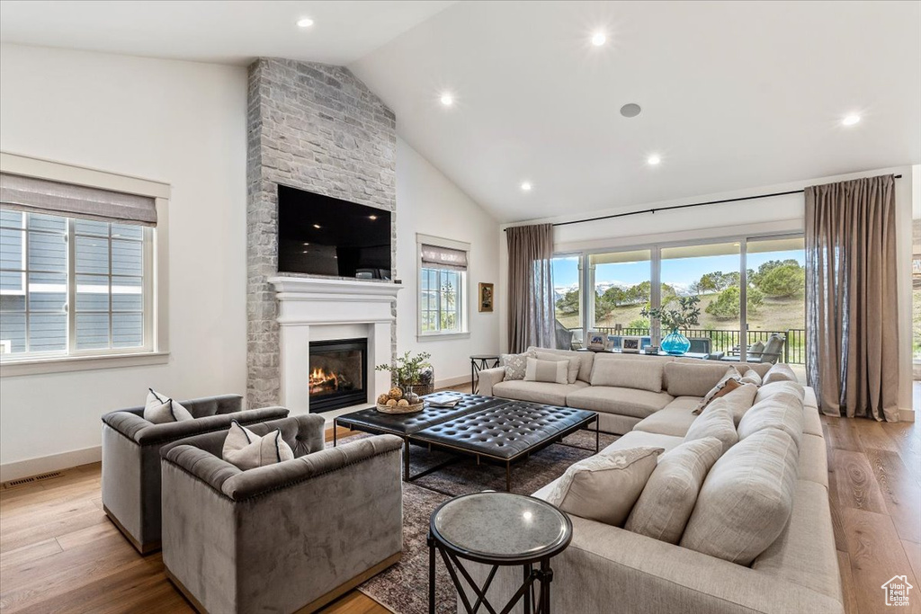 Living room with light wood finished floors, a fireplace, high vaulted ceiling, and recessed lighting