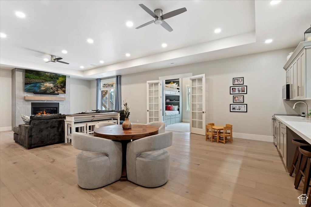Dining space featuring a ceiling fan, light wood-style flooring, a large fireplace, recessed lighting, and a raised ceiling