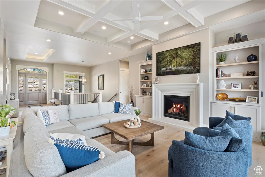 Living room with coffered ceiling, light wood-style flooring, recessed lighting, beam ceiling, and a glass covered fireplace