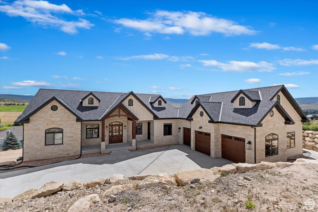 French country style house with stone siding, board and batten siding, driveway, and an attached garage