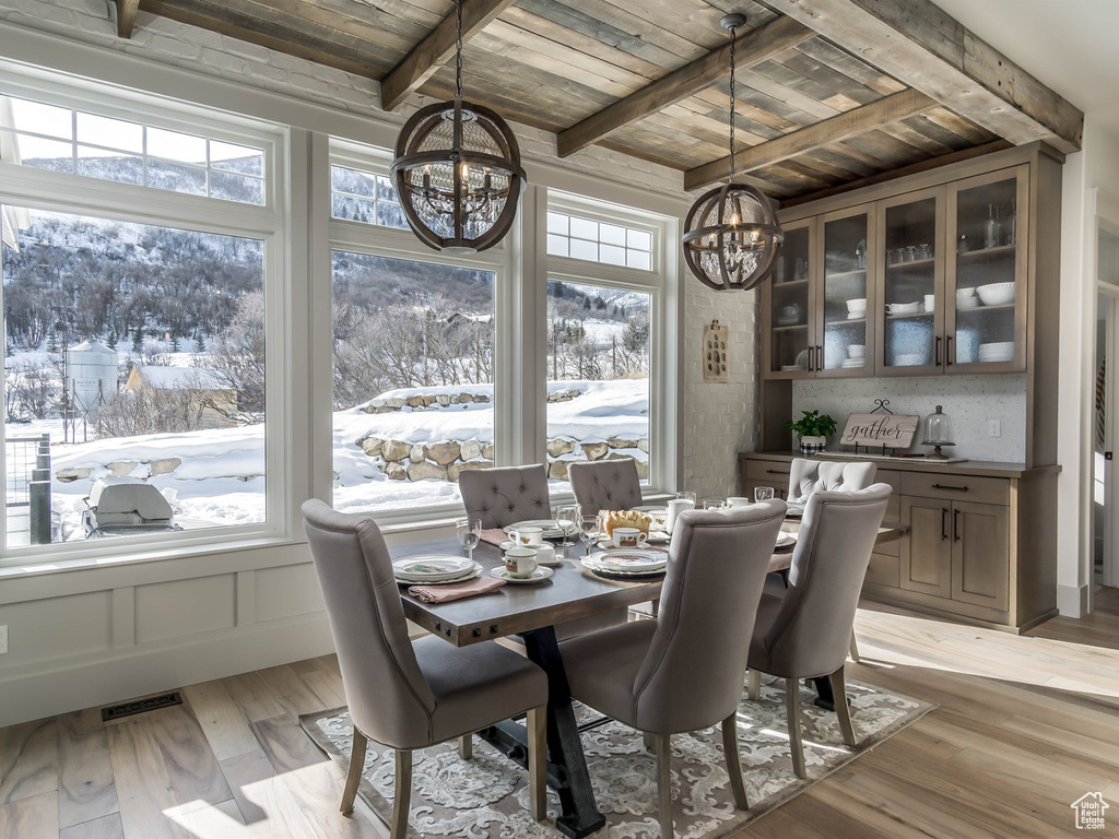 Dining space with a chandelier, a wooden ceiling with exposed beams, healthy amount of natural light, and light wood-style floors