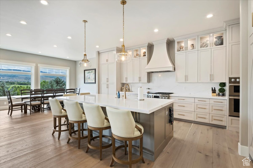Kitchen with custom range hood, light countertops, recessed lighting, an island with sink, and a breakfast bar