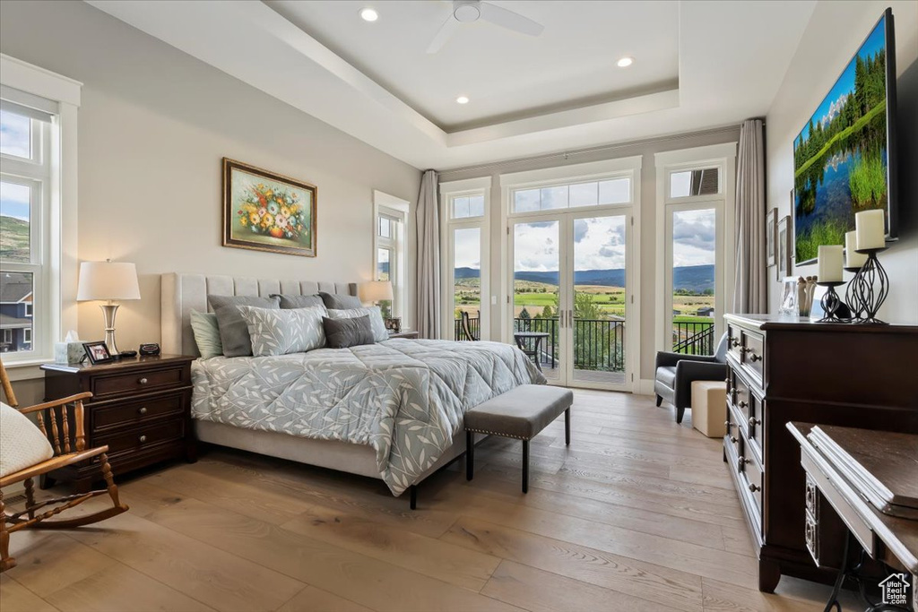 Bedroom featuring access to exterior, light wood finished floors, a tray ceiling, recessed lighting, and a ceiling fan