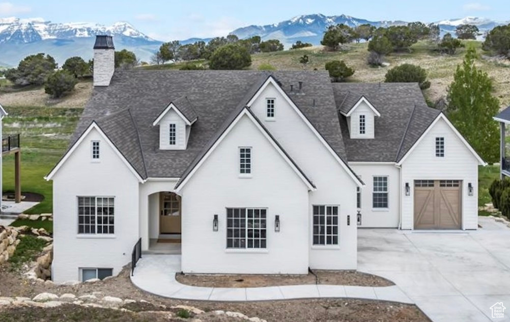View of front of property featuring a mountain view, concrete driveway, a shingled roof, and a chimney