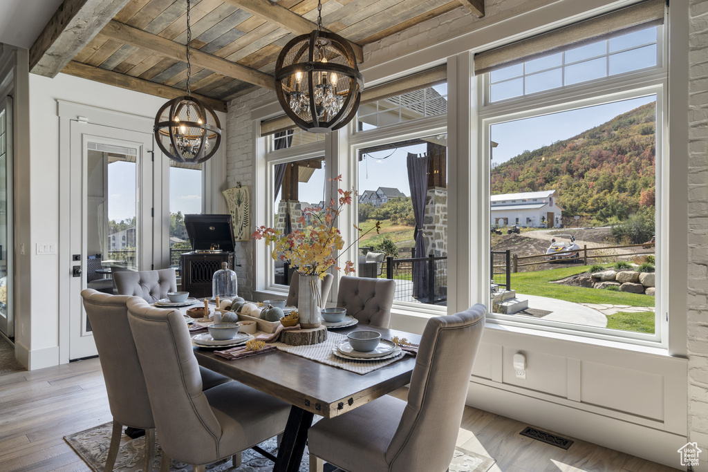 Dining space with a chandelier, a wooden ceiling with exposed beams, plenty of natural light, and wood finished floors