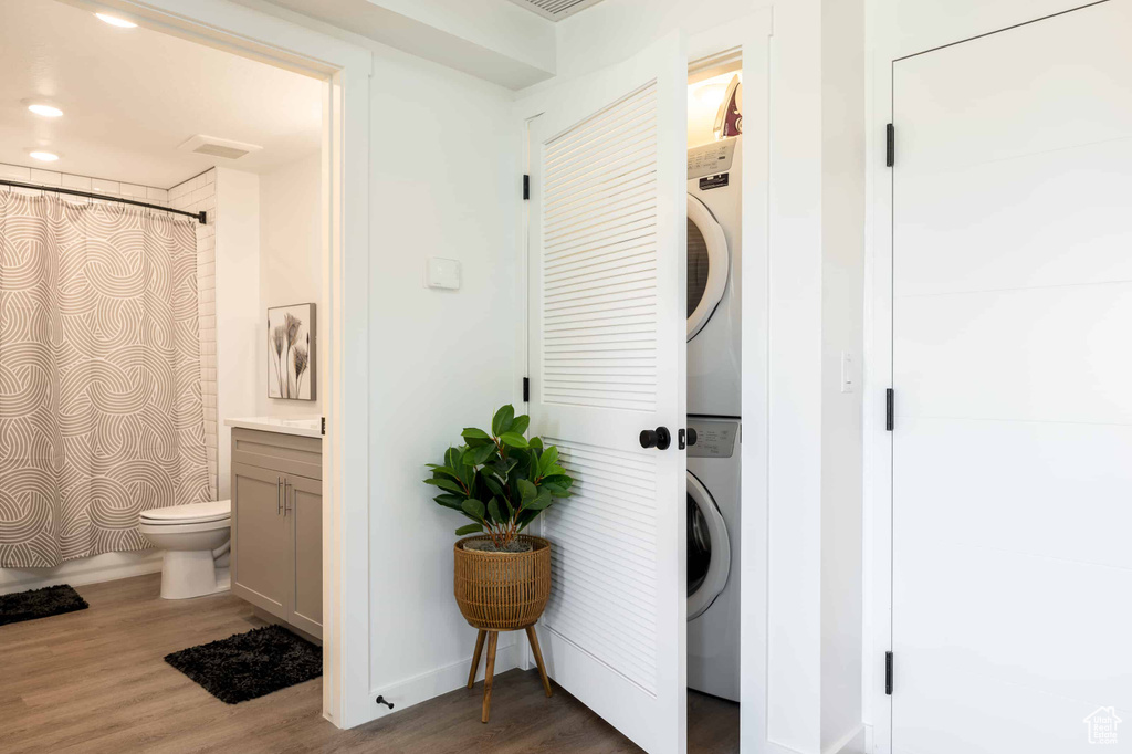 Laundry room with stacked washer and clothes dryer and wood finished floors