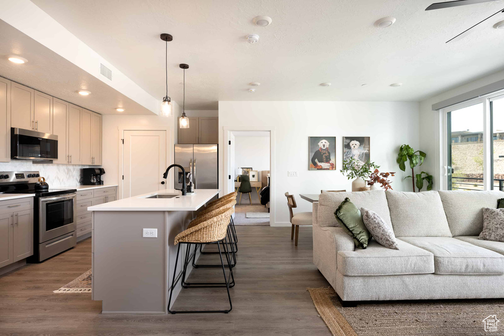 Kitchen featuring stainless steel appliances, open floor plan, a kitchen bar, backsplash, and wood finished floors