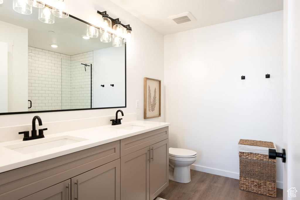 Full bathroom featuring double vanity, wood finished floors, and a tile shower