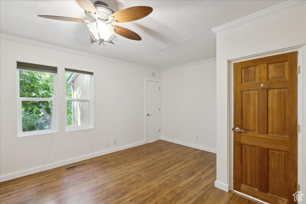 Spare room with wood finished floors, crown molding, a ceiling fan, and a textured ceiling