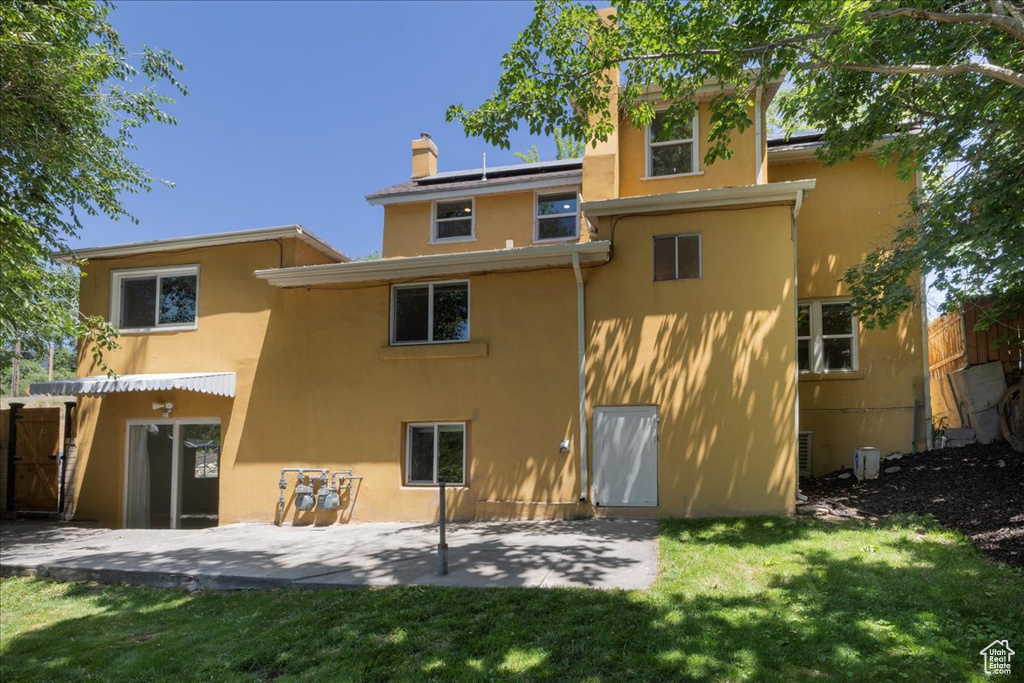 Back of property featuring stucco siding, a patio, solar panels, a yard, and a chimney