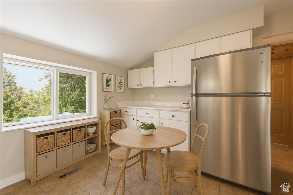 Kitchen with freestanding refrigerator, lofted ceiling, light countertops, white cabinetry, and light tile patterned floors