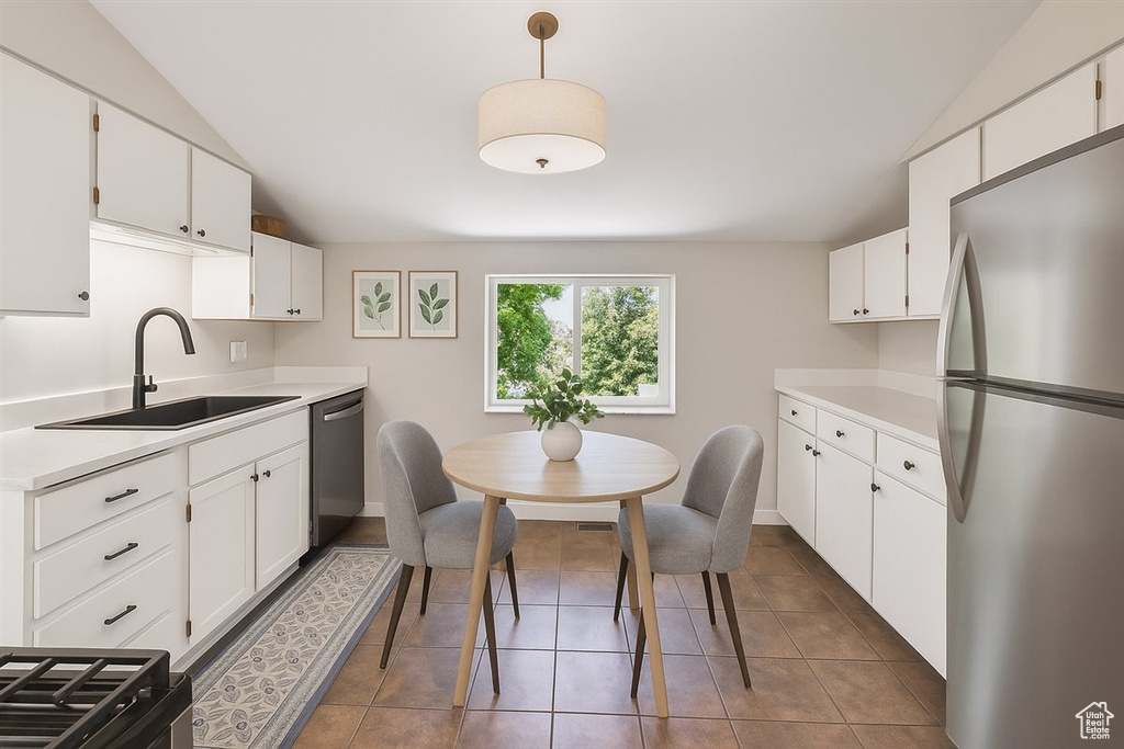 Kitchen featuring stainless steel appliances, vaulted ceiling, light countertops, white cabinets, and tile patterned flooring