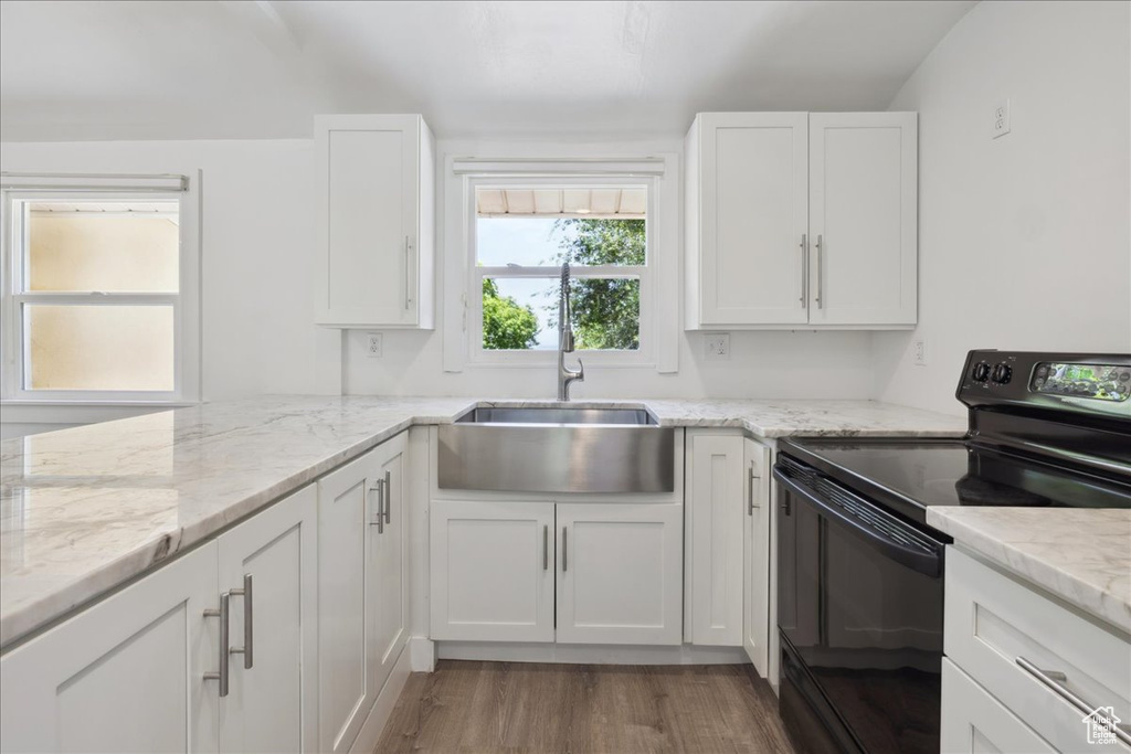 Kitchen with black electric range, white cabinets, wood finished floors, and light stone countertops