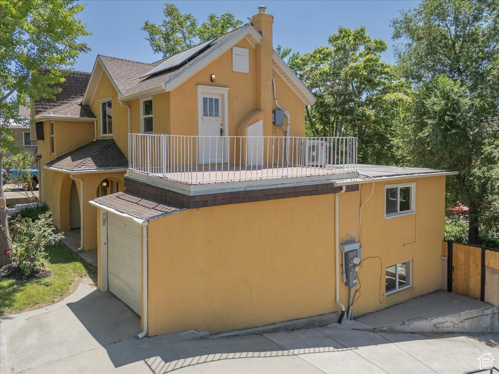 Rear view of property featuring a balcony, roof mounted solar panels, stucco siding, and a chimney