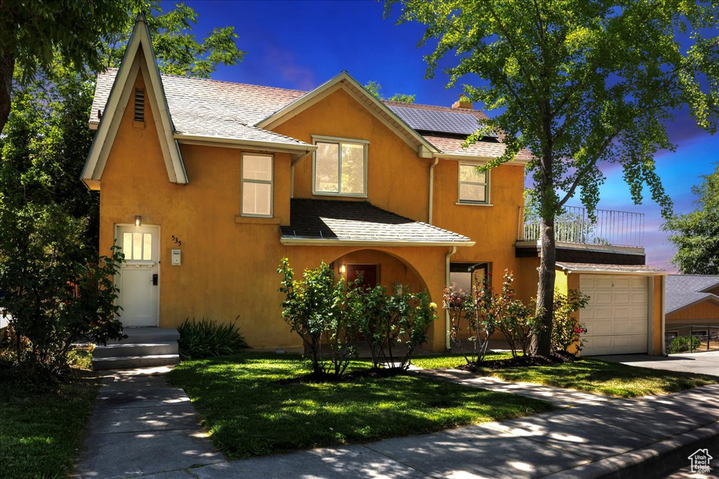 View of front of home featuring stucco siding, roof mounted solar panels, concrete driveway, a front yard, and a balcony