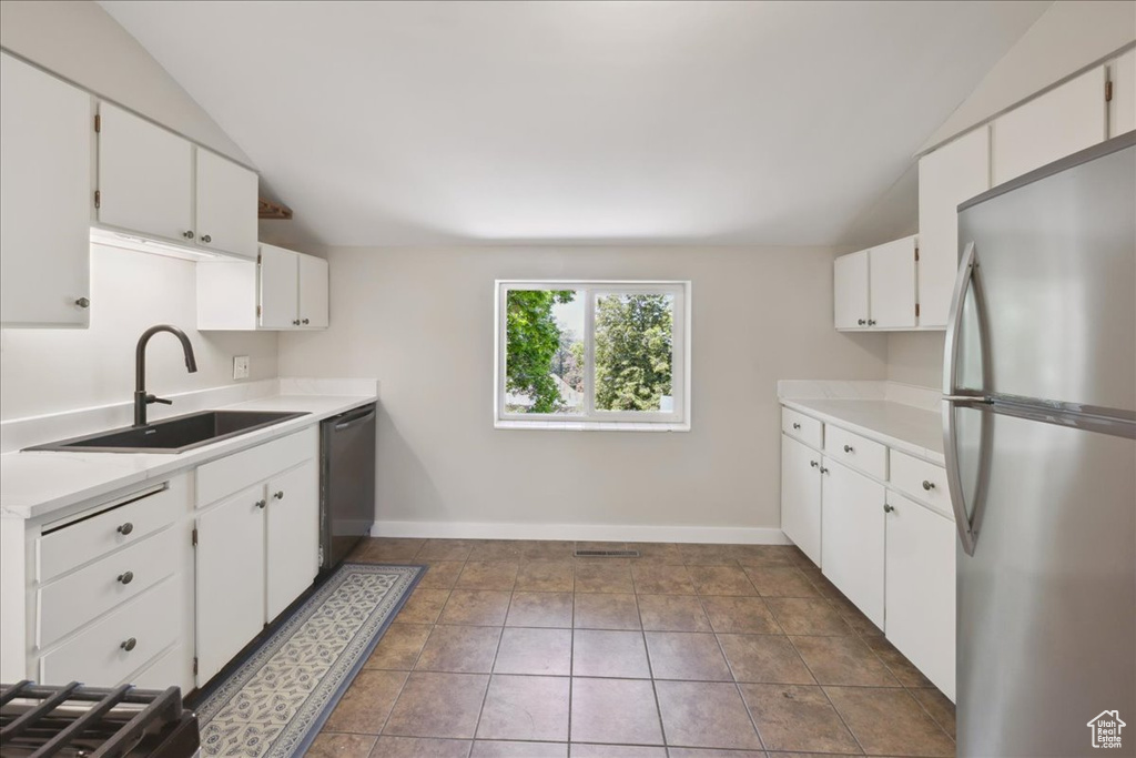 Kitchen featuring stainless steel appliances, vaulted ceiling, light countertops, and white cabinets