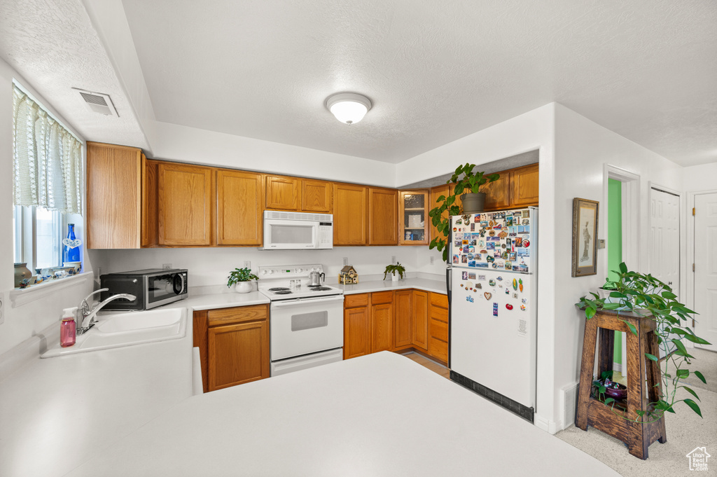Kitchen featuring white appliances, light countertops, glass insert cabinets, a textured ceiling, and brown cabinetry
