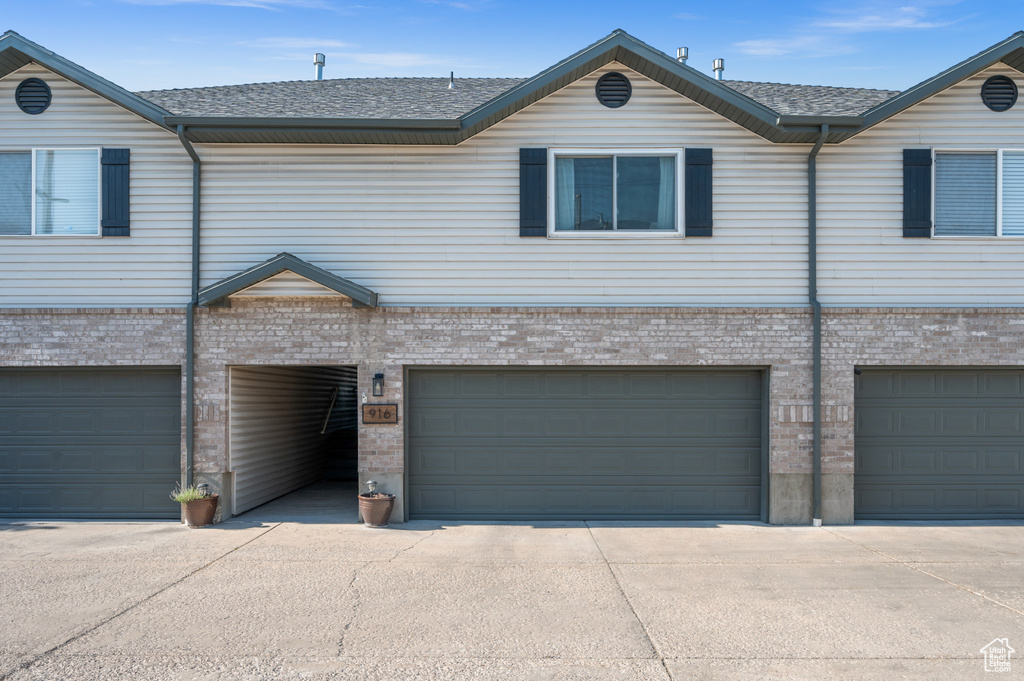 View of front of home with brick siding, a garage, concrete driveway, and a shingled roof