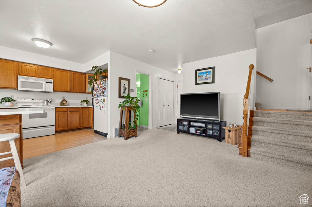 Kitchen with white appliances, light carpet, brown cabinetry, light countertops, and open floor plan