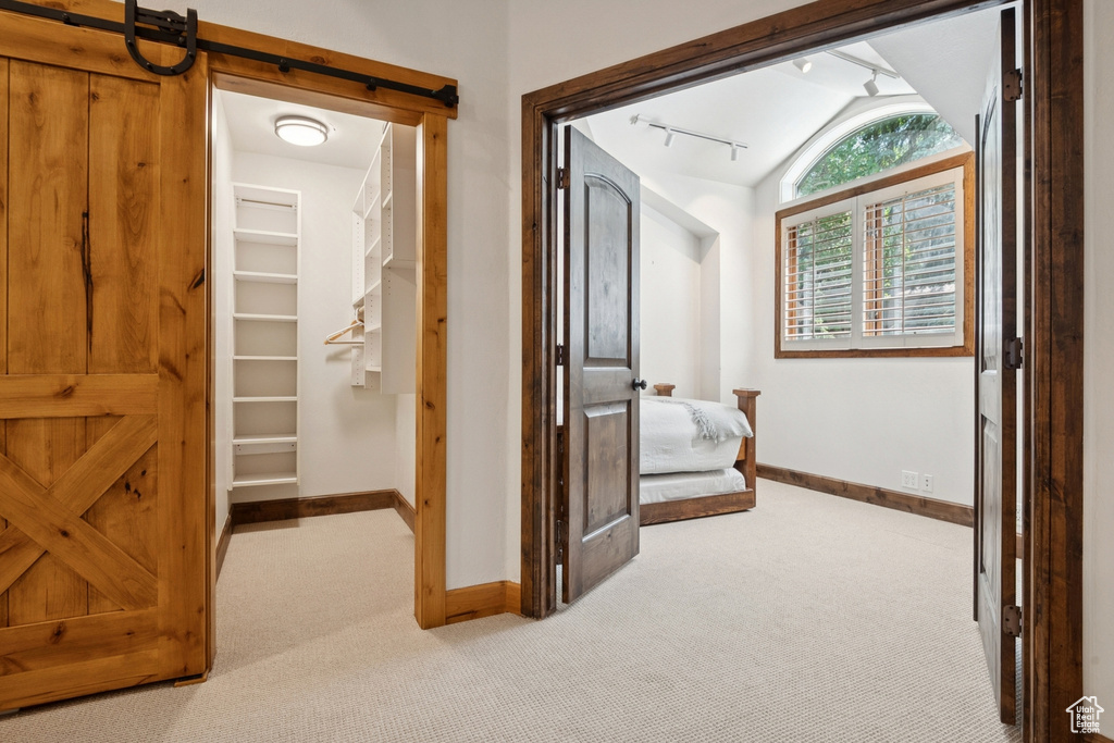 Hallway with carpet, vaulted ceiling, a barn door, and rail lighting