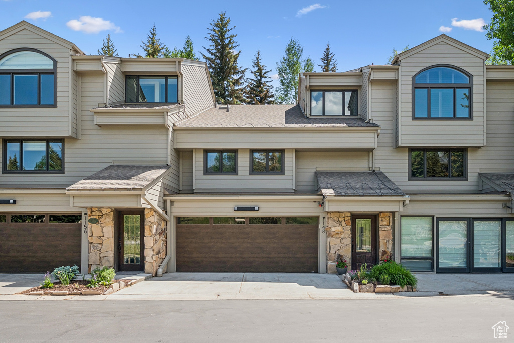 Multi unit property featuring an attached garage, stone siding, and driveway