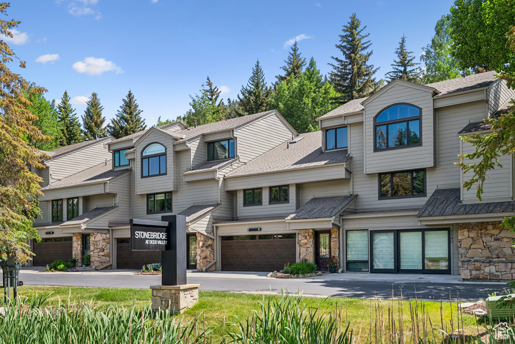 Multi unit property featuring stone siding, a garage, and a shingled roof