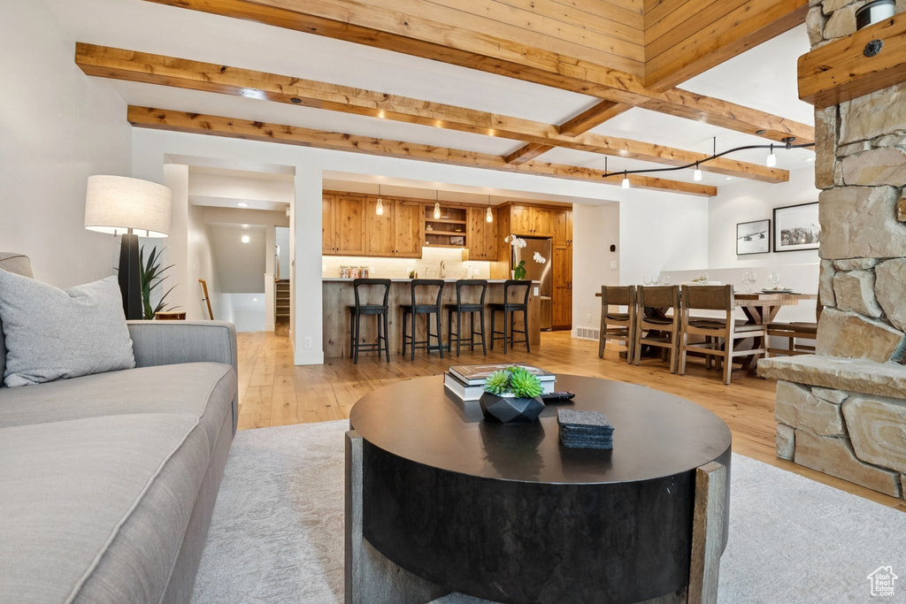 Living area featuring light wood-type flooring, beam ceiling, and bar with sink