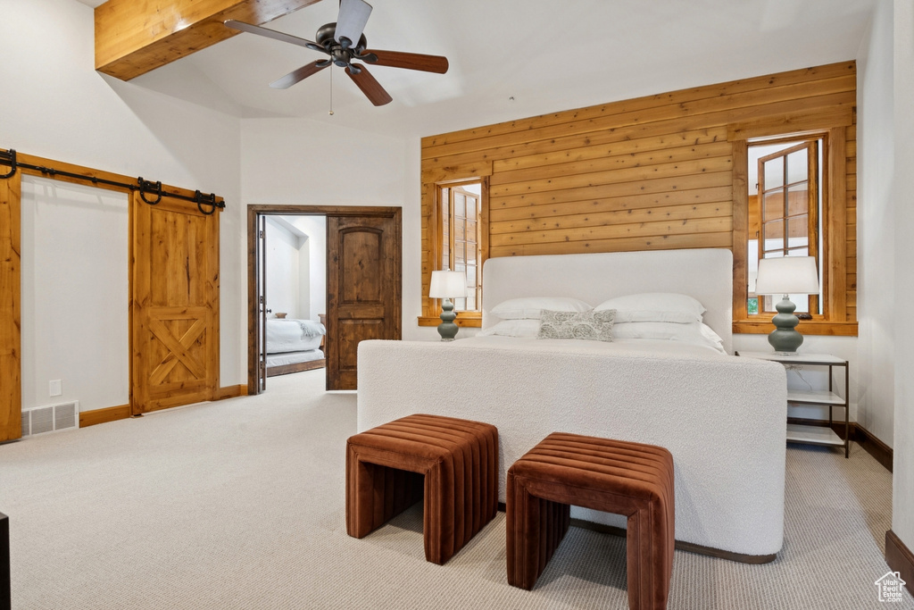 Bedroom featuring a barn door, light carpet, wooden walls, a ceiling fan, and beam ceiling