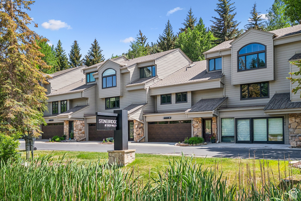 Townhome / multi-family property with stone siding, a garage, driveway, and roof with shingles