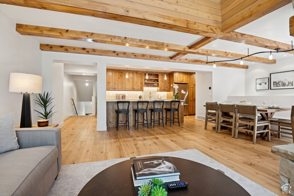 Living room featuring wet bar, beam ceiling, and light wood-style floors