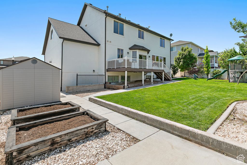 Rear view of property featuring a shed, a playground, a lawn, a wooden deck, and stucco siding