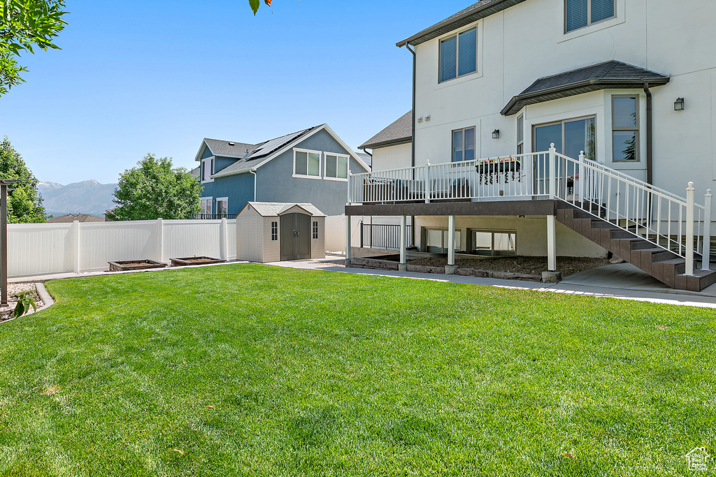 Rear view of property featuring a deck, a storage unit, a fenced backyard, stucco siding, and stairs