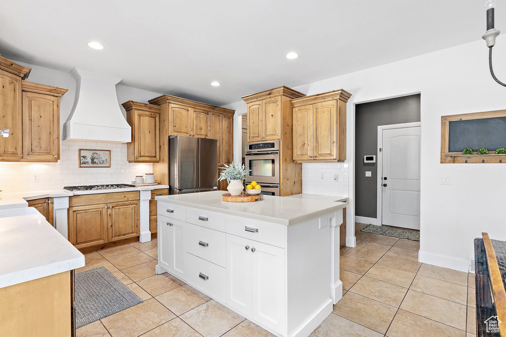 Kitchen featuring appliances with stainless steel finishes, wall chimney exhaust hood, tasteful backsplash, light tile patterned floors, and light countertops