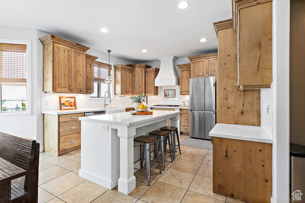 Kitchen featuring stainless steel appliances, premium range hood, a kitchen island, tasteful backsplash, and a kitchen bar