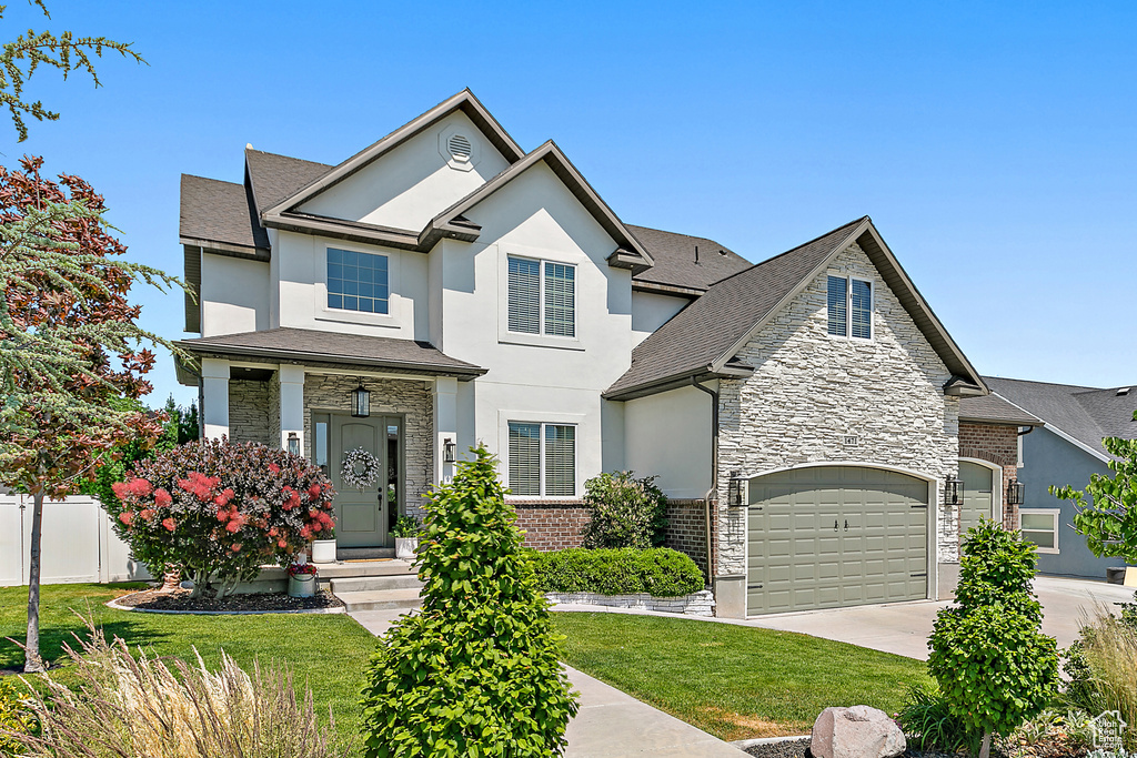 View of front of home with stone siding, stucco siding, concrete driveway, and a shingled roof
